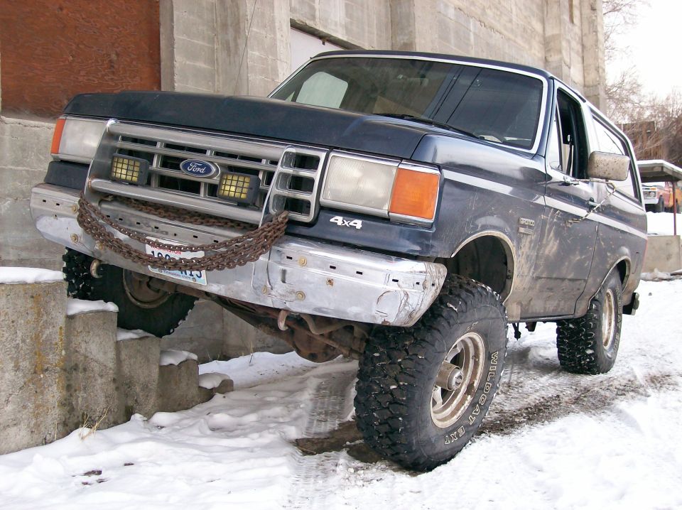 1988 Ford Bronco 4x4 with chains on front bumper, driving over concrete blocks in snow