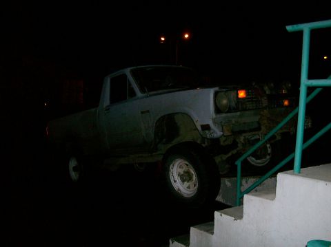 1988 Ford Bronco - A light-colored pickup truck is parked precariously on a set of stairs at night.