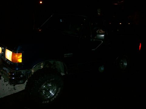 1988 Ford Bronco - A dark blue Ford Bronco with off-road tires is parked at night, showing its front-left side.