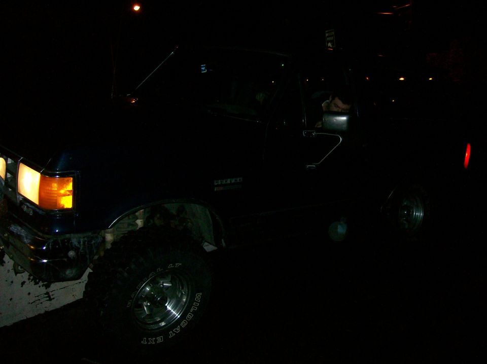 Dark blue Ford Bronco with lifted suspension and off-road tires, seen at night