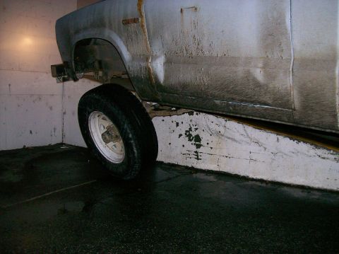 1988 Ford Bronco - A dirty white Ford Courier truck is seen from the side, raised on blocks in a garage.