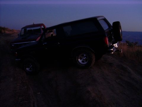 1988 Ford Bronco - Two trucks are parked on a dirt incline as the sky darkens.