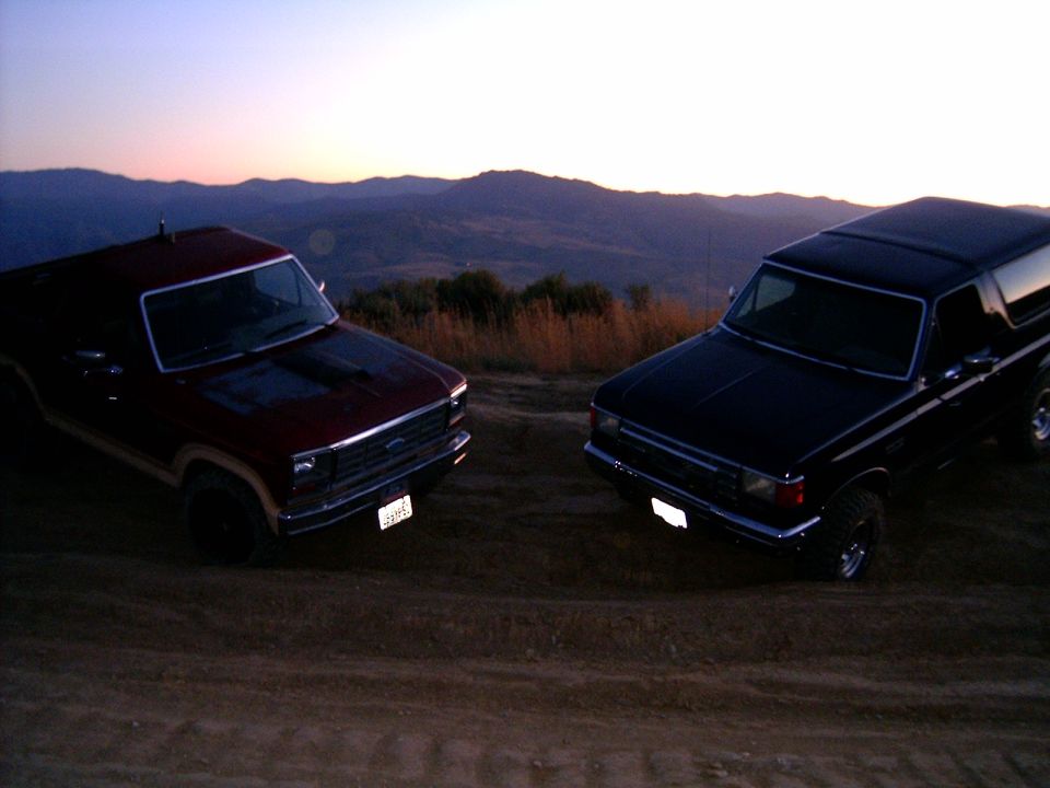 Two 1988 Ford Broncos parked on a dirt hill at sunset