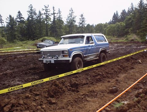 1985 Ford Bronco - A 1985 Ford Bronco navigates a muddy course, with another vehicle visible in the background.