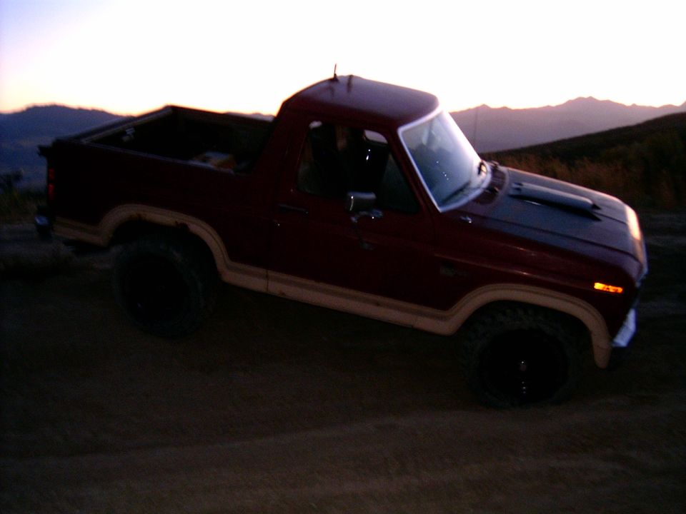 Maroon Ford Bronco with tan trim and black hood scoop, parked on dirt