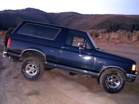 1988 Ford Bronco - A dark blue Ford Bronco is parked on a dirt road with hills in the background.