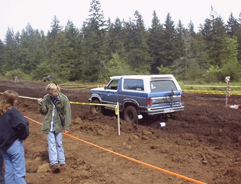 1985 Ford Bronco - Ford Bronco navigates a muddy off-road course with spectators present.