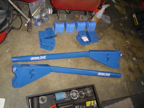 1978 Ford Bronco - Various blue suspension parts laid out on a concrete floor, including control arms and brackets.