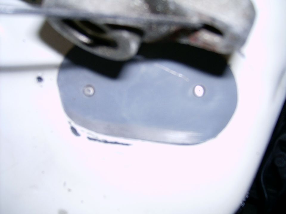 Close-up of a car's white body panel with a gray, oval-shaped patch secured by two rivets