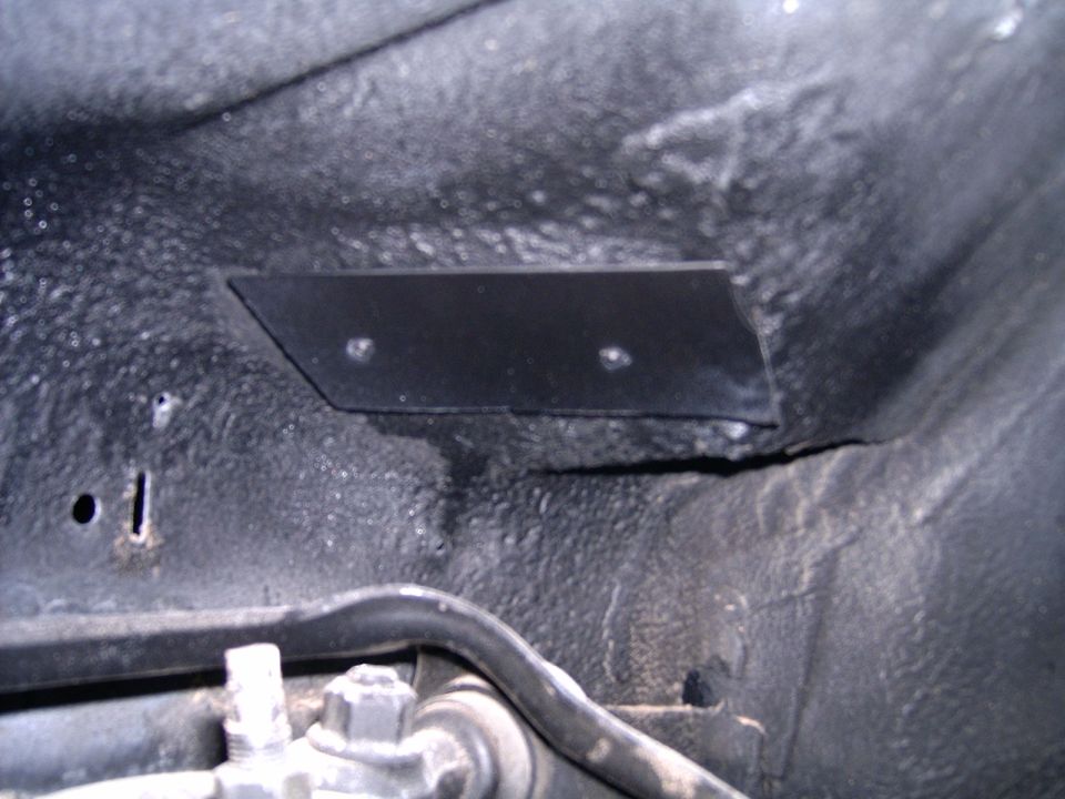Black metal plate with two holes bolted to a textured, dark undercarriage