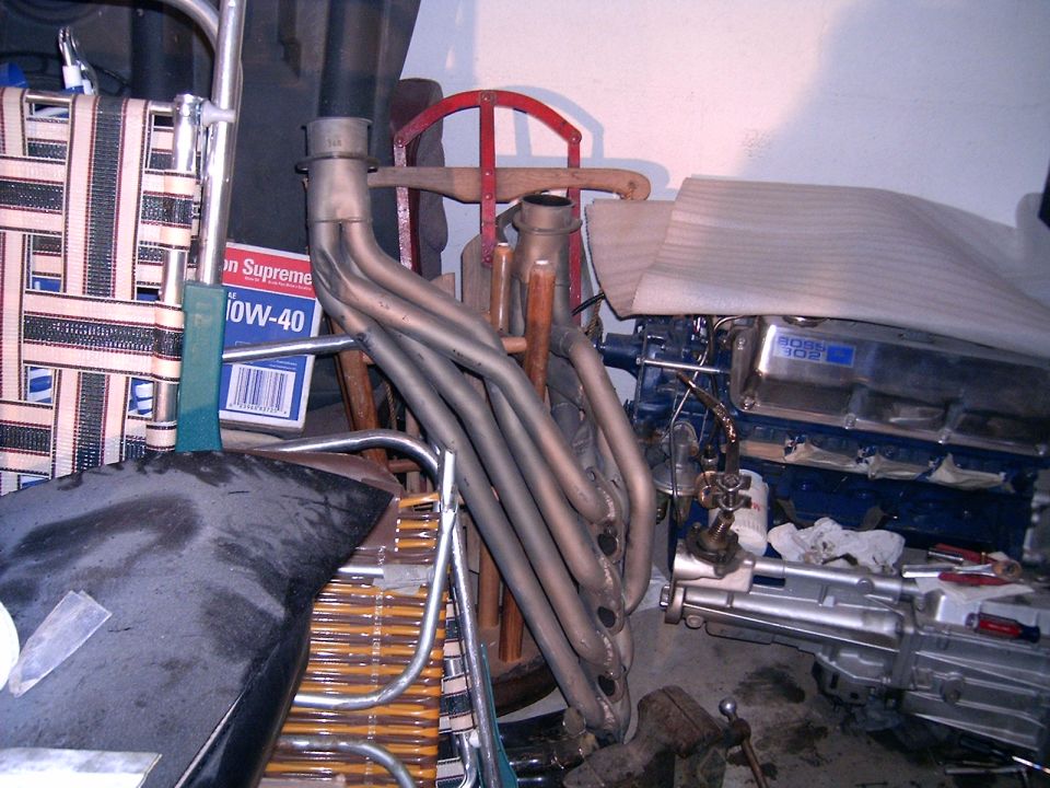 Engine with blue valve covers and chrome intake manifold, next to exhaust headers and a box of oil