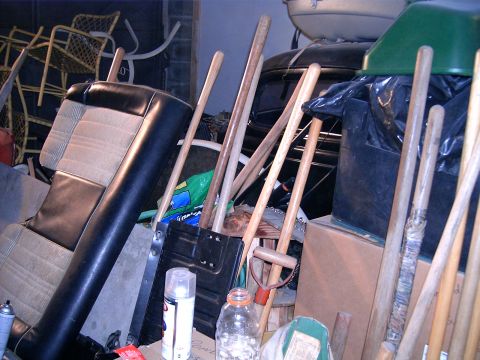 1978 Ford Mustang II - A car seat and a collection of gardening and sports tools are stored together in a disorganized area.