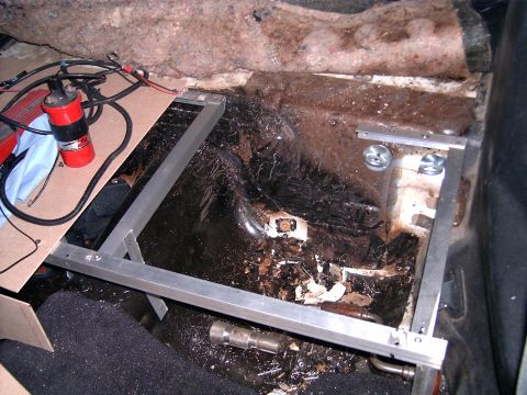 1978 Ford Mustang II - Interior view of a car's floor showing damage and custom metal brackets, with an ignition coil present.