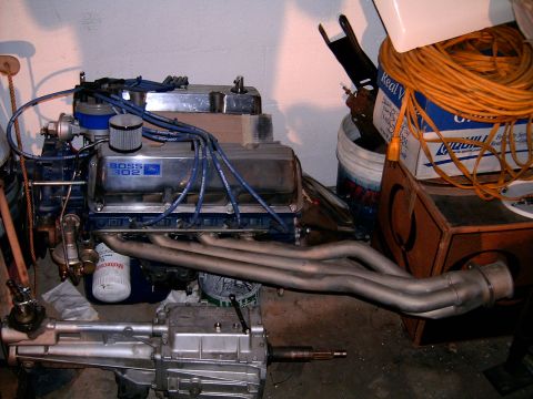 1978 Ford Mustang II - A Ford Boss 302 engine assembly, including headers and a transmission, is shown in a workshop setting with various items in the background.