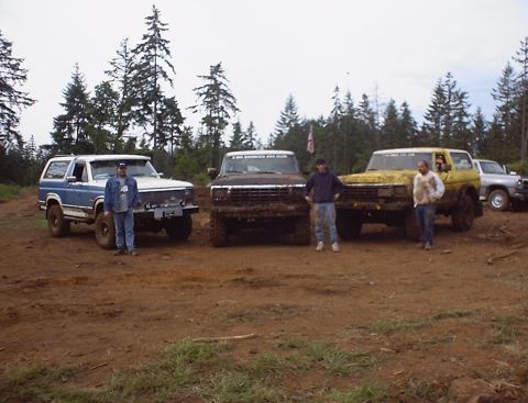 1985 Ford Bronco - A group of four-wheel-drive vehicles and their drivers pose in a muddy outdoor setting.