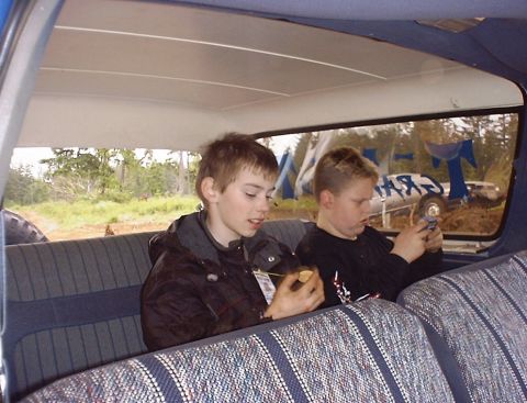 1985 Ford Bronco - Boys ride in the back seat of a vehicle, with a glimpse of the outdoors and another vehicle outside.