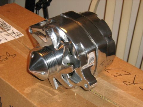 1988 Mercury Grand Marquis - A polished chrome/billet-finish alternator sitting on a taped cardboard shipping box indoors, shown from the pulley-nose end with its finne…