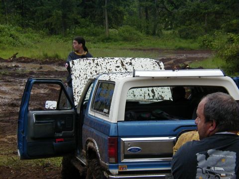 1985 Ford Bronco - A mud-covered Ford Bronco sits in a muddy, wooded area with its driver's door ajar.