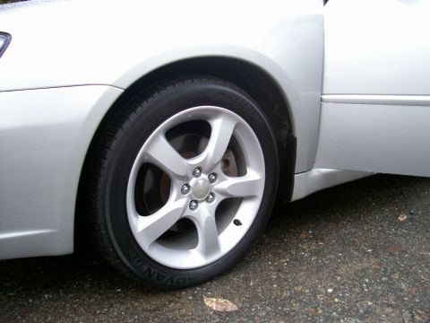 2001 Ford Crown Victoria - Close-up of a silver car's wheel and lower body panel, showing the front tire and part of the open driver's side door.