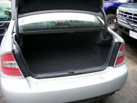 2001 Ford Crown Victoria - The rear of a silver sedan is shown with its trunk open, revealing the cargo area. Other vehicles are visible behind it.