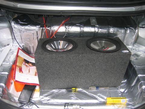 1996 Ford Crown Victoria - The trunk of a car is lined with sound insulation and contains a dual subwoofer box and various tools.