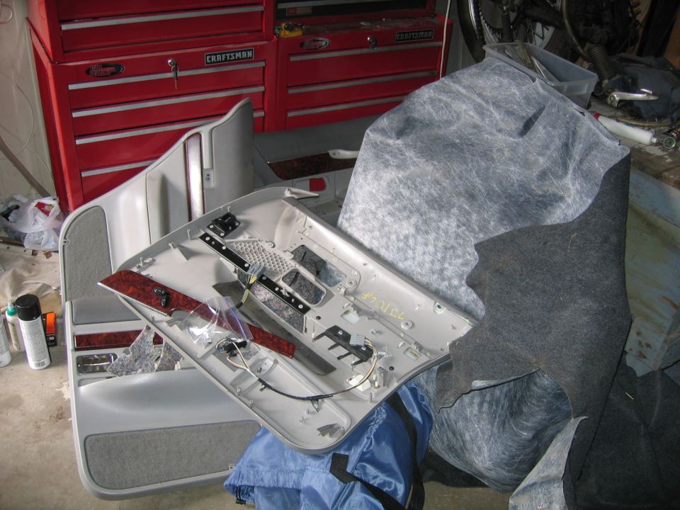 Car door panel disassembled, showing interior components and insulation material. Red Craftsman tool chest in background