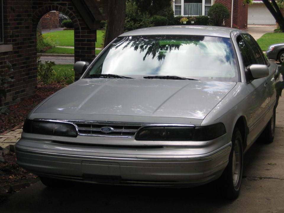 Silver sedan, front view, parked in driveway. Chrome grille with Ford emblem, dark headlights, chrome bumper