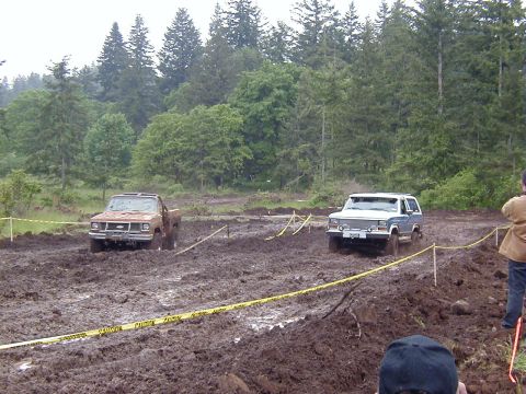1985 Ford Bronco - Two SUVs tackle a challenging mud course, demonstrating their off-road capabilities.