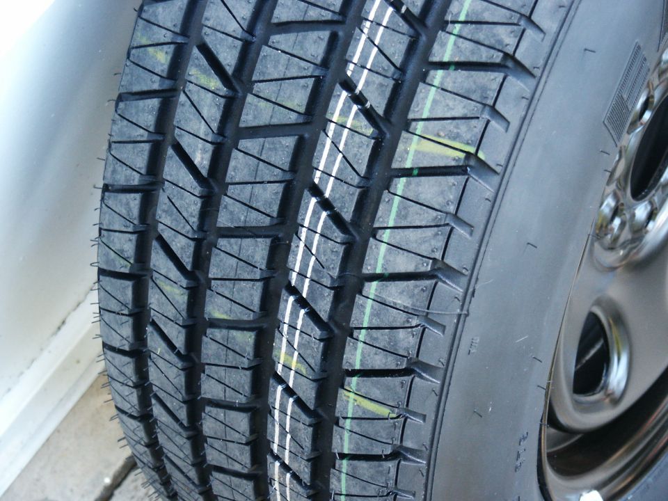 Close-up of a tire with a distinct tread pattern and white and green markings. A silver rim is visible on the right