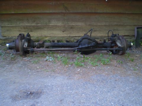 1979 Ford Bronco - A rear axle assembly is shown outdoors against a wooden wall, with grass and dirt visible.