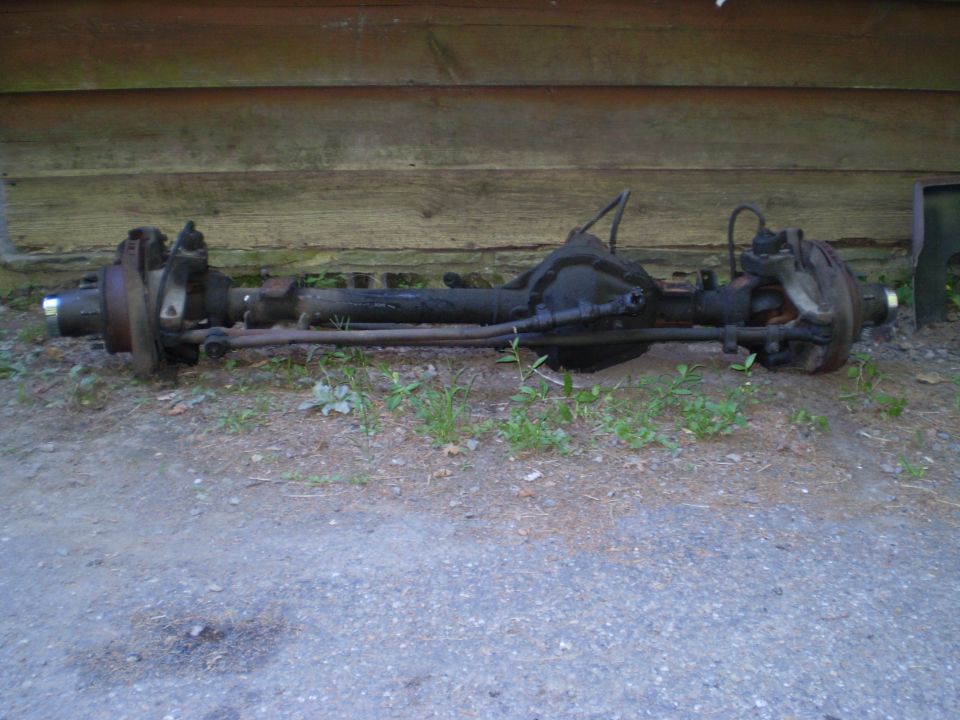 Rear axle assembly with drum brakes and suspension components, resting on dirt and gravel