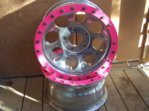 1989 Ford Bronco - A pair of chrome wheels with bright pink trim and visible lug nuts are stacked on a wooden surface.