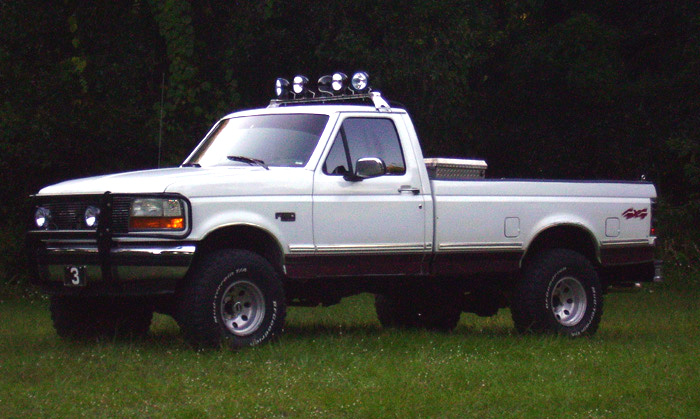 White and maroon Ford F-150 pickup truck with off-road lights on roof, parked on grass
