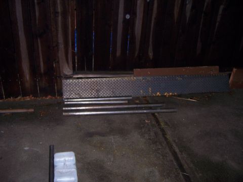 1991 Ford Bronco - Metal sliders and pipes are laid out on a concrete floor in front of a wooden fence.