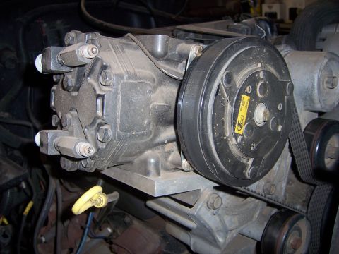 1991 Ford Bronco - Close-up view of an air conditioning compressor, likely from an older vehicle, with a yellow label visible on the pulley.