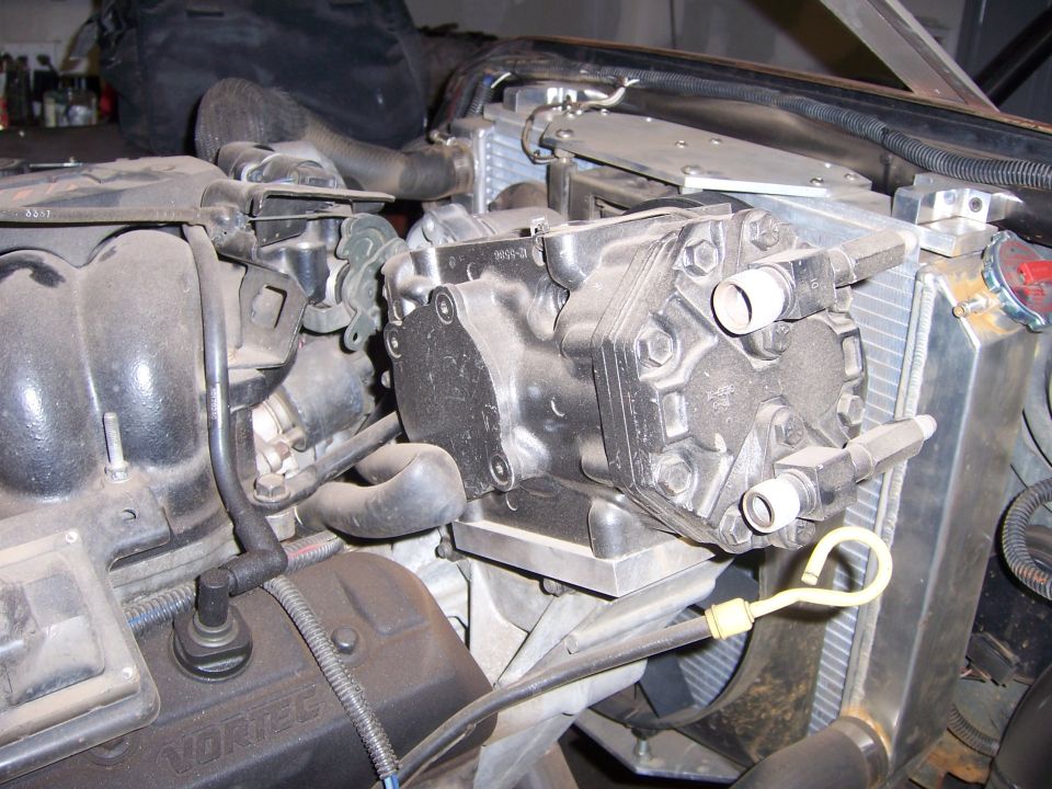 Engine bay showing an air conditioning compressor mounted near the radiator. Oil dipstick is visible