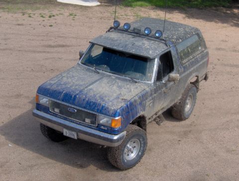 1987 Ford Bronco - A muddy 1987 Ford Bronco is viewed from a high angle, equipped with auxiliary lights on its roof.