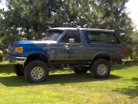 1987 Ford Bronco - This lifted Ford Bronco features a custom paint job with blue flames and auxiliary lights on the roof.
