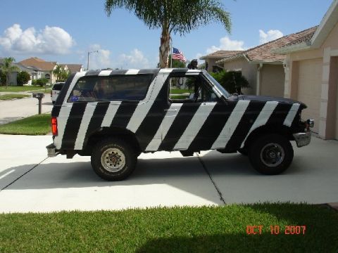 1996 Ford Bronco - A Ford Bronco with a distinctive black and white stripe paint job is parked in front of a suburban house.