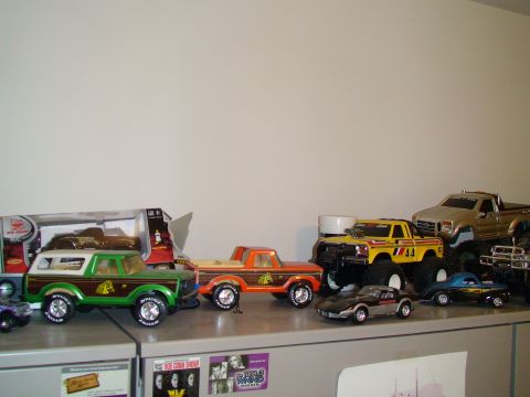 1979 Ford Bronco - A collection of toy vehicles, including a green and brown 1979 Ford Bronco with wood paneling, are displayed on a shelf.