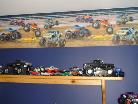 1979 Ford Bronco - A collection of monster truck toys displayed on a shelf, with a mural of monster trucks in action on the wall.