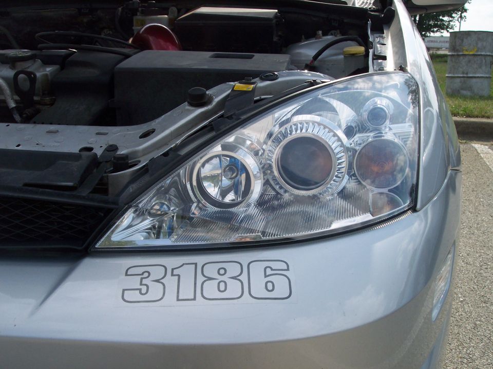 2003 Ford Focus front passenger side headlight assembly and part of the engine bay. Number 3186 is on the bumper