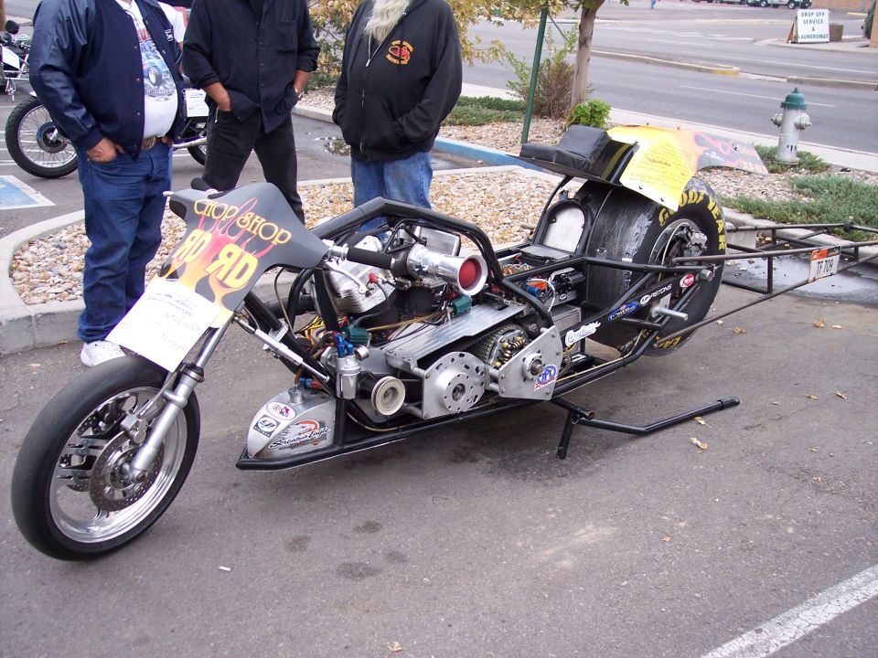 Drag racing motorcycle with exposed engine and large rear tire, parked outdoors