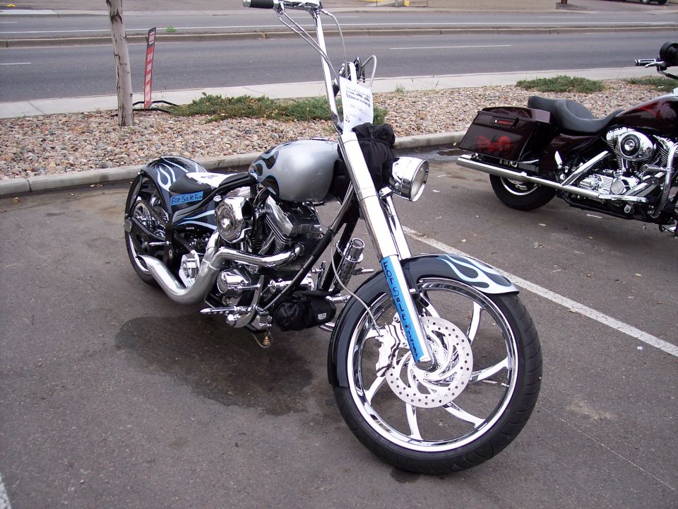 Silver chopper motorcycle with blue flames and chrome wheels, parked next to another motorcycle
