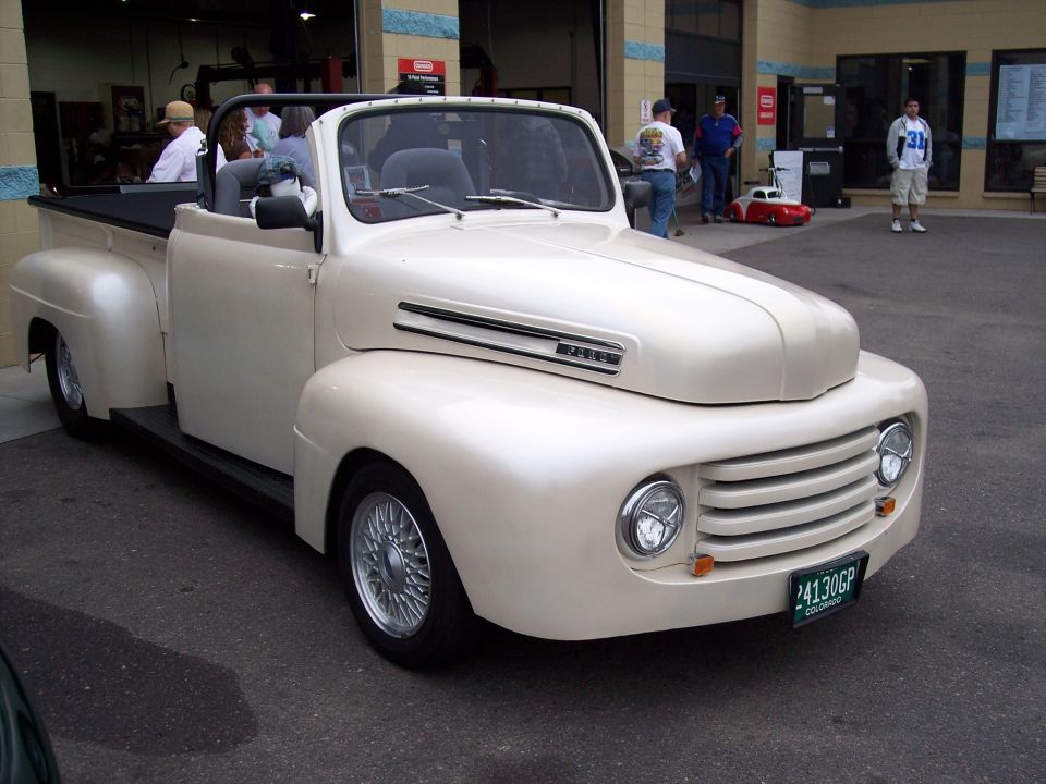 Cream-colored convertible pickup truck with a black soft top, chrome grille, and wire-spoke wheels