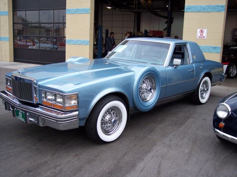 1972 Ford Ranchero - A light blue coupe with whitewall tires and wire wheels is parked in front of a garage, with another car visible to the right.