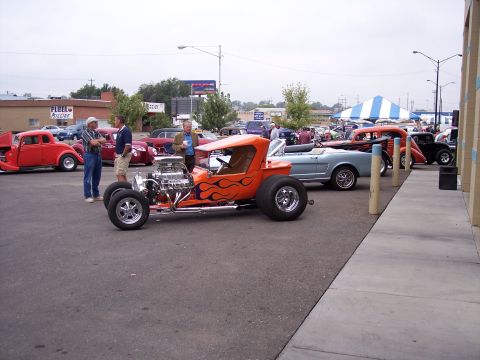 1972 Ford Ranchero - Several custom and classic cars are on display at an outdoor event, with a prominent orange hot rod in the foreground.