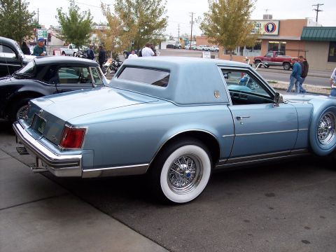 1972 Ford Ranchero - A light blue 1977 Cadillac Eldorado coupe is parked next to a dark car, with people and buildings in the background.