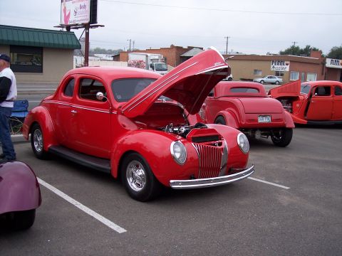 1972 Ford Ranchero - A bright red 1940s coupe is parked with its hood open, displaying the engine, alongside other red vehicles.