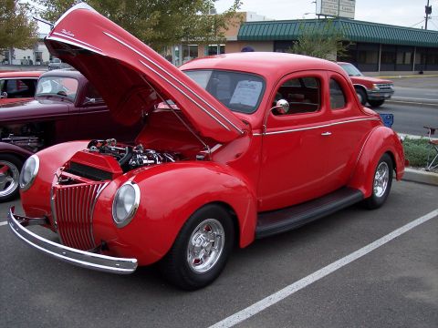 1972 Ford Ranchero - A bright red 1940 Ford coupe is displayed with its hood open, revealing the engine. Another classic car is visible to the left.
